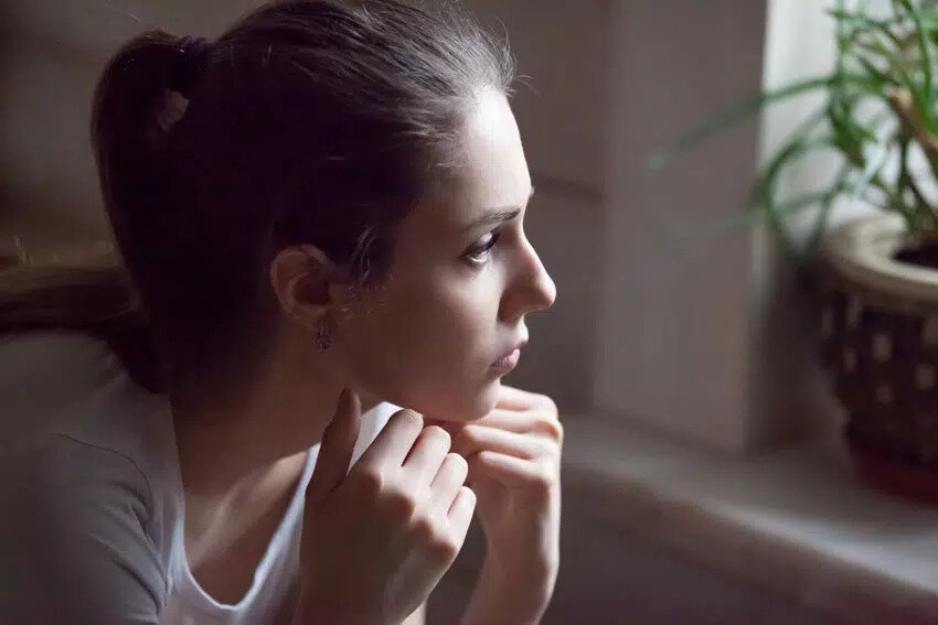 woman looking out the window with a blank stare, resting her chin on her knuckles