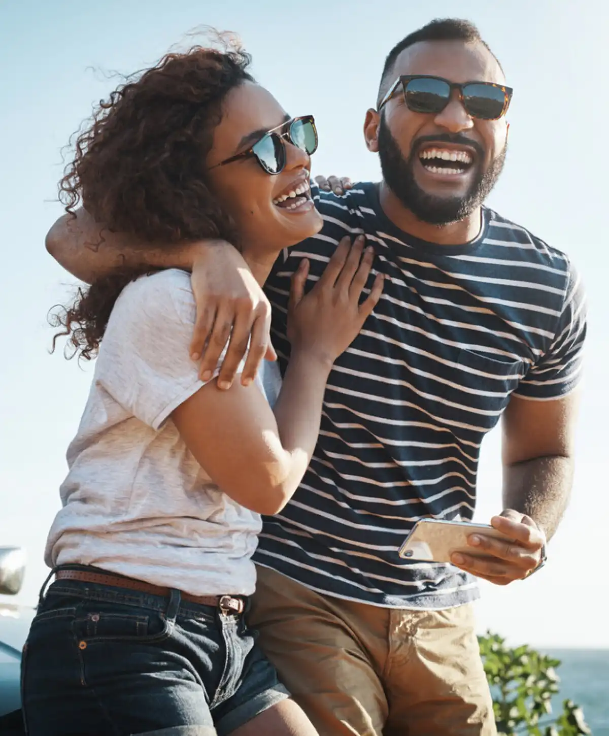Laughing couple in sunglasses embraces outdoors by the ocean